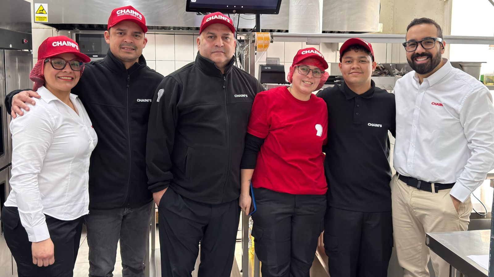 Equipo de CHAINI'S en la cocina junto a la pantalla de KDS