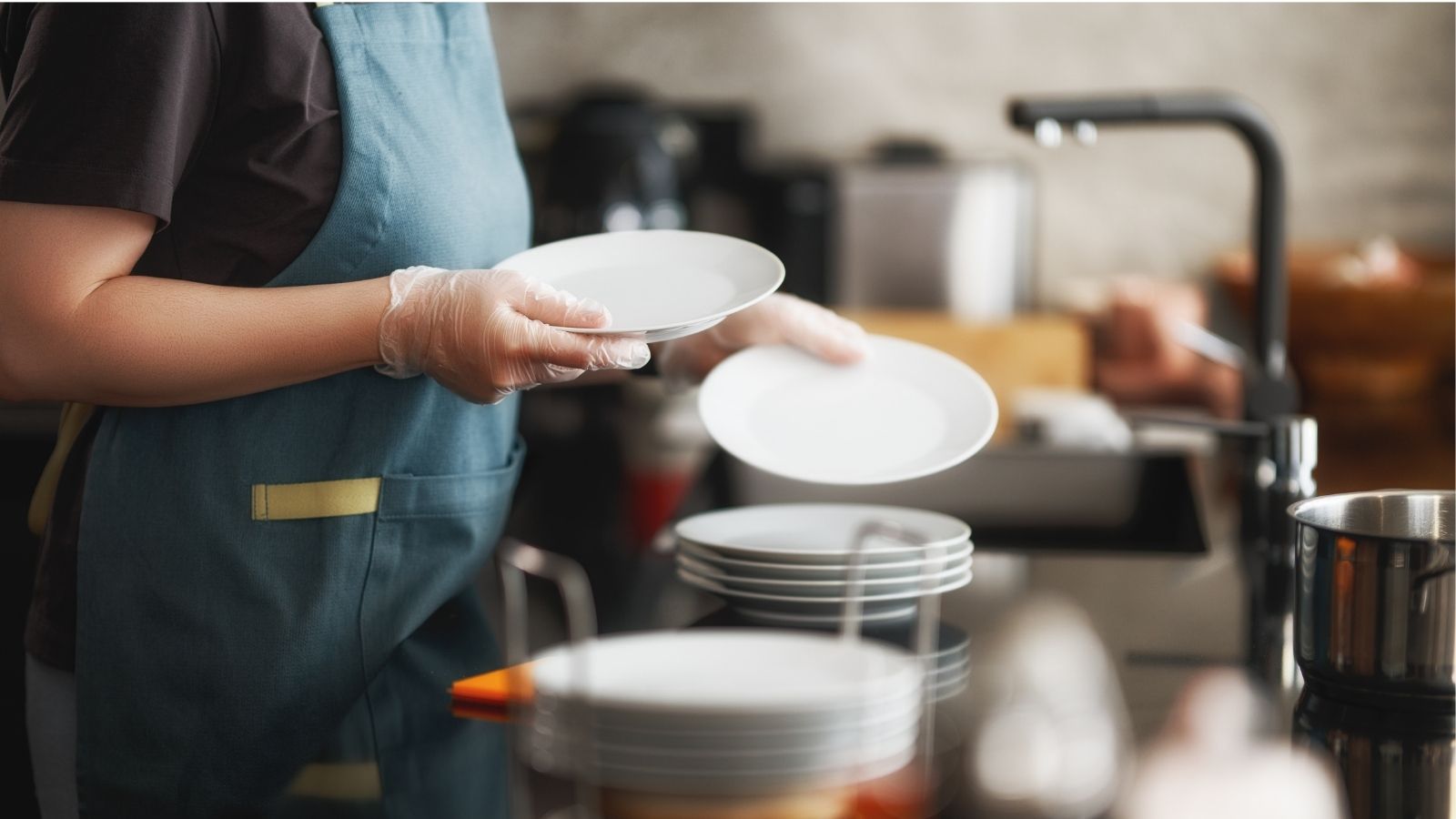 Checklist sanitario para restaurantes, trabajadora de cocina con guantes ordena platos limpios junto al lavaplatos