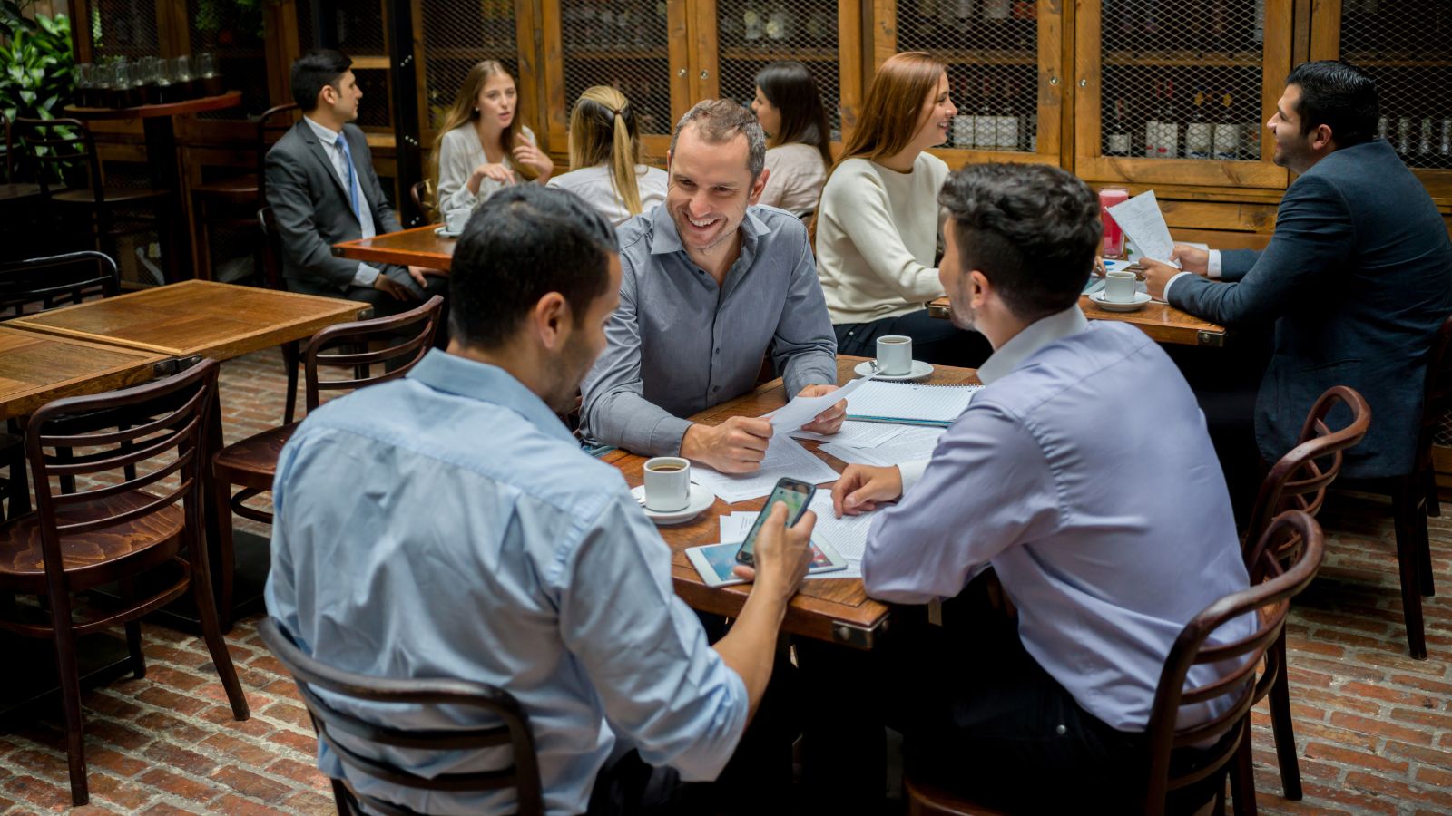 Tres personas reunidas en la mesa de un restaurante con papeles, café y un cuaderno mientras conversan un acuerdo