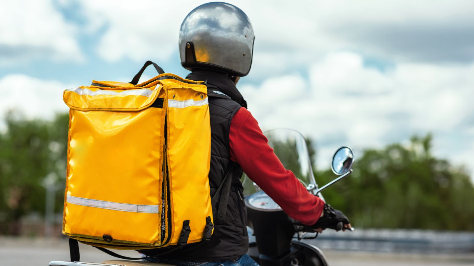 Delivery propio o tercerizado, repartidor en moto con mochila térmica amarilla saliendo a entregar