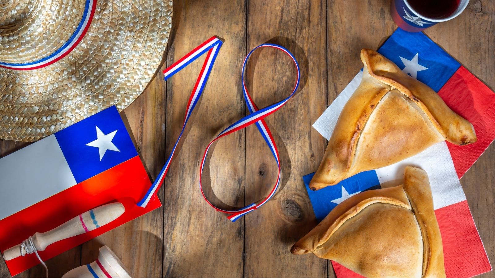 Oferta de Fiestas Patrias, empanadas, banderas chilenas y una chupalla sobre una mesa de madera