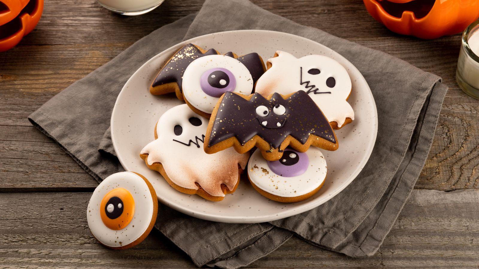 Plato con galletas decoradas de Halloween con forma de fantasma, murciélago y ojo sobre una mesa de madera