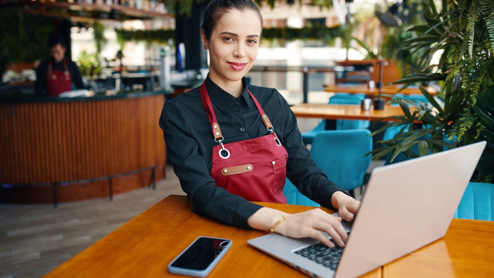 Redes sociales de un restaurante sin community manager, trabajadora del local con delantal usando un notebook en el salón